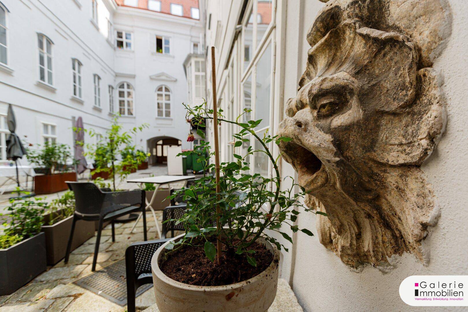 Ruhiger Innenhof mit Sitzgelegenheiten, Pflanzen und einer dekorativen Steinskulptur an der Wand.