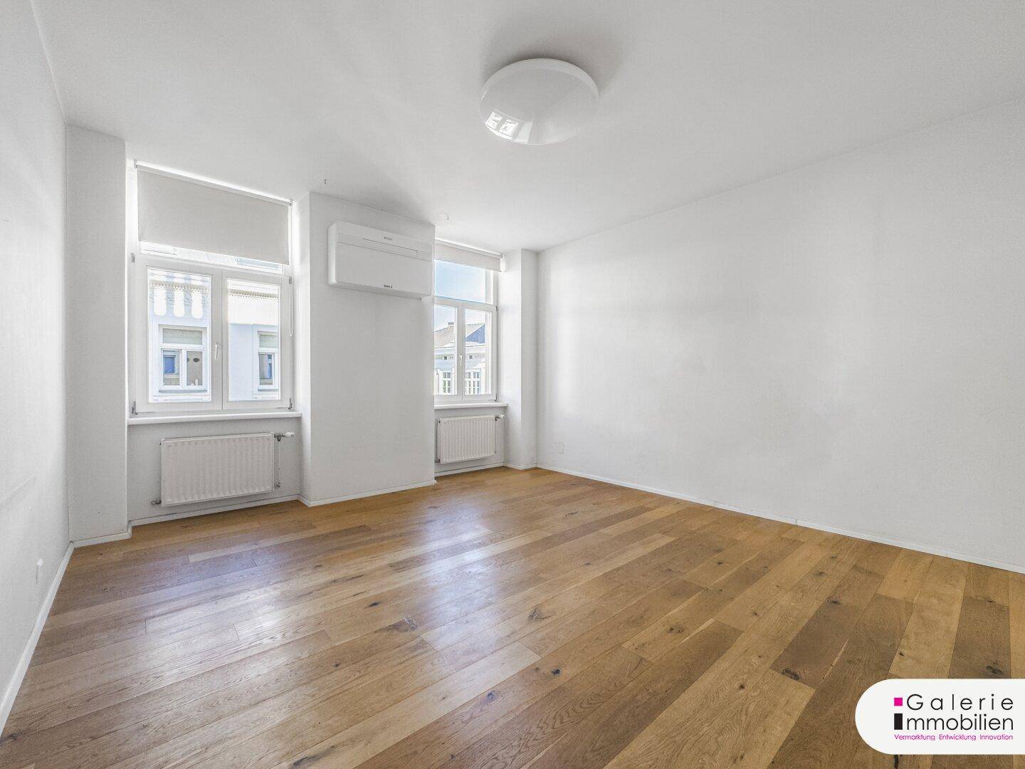 Heller Raum mit Holzparkett, Klimaanlage und großen Fenstern, ideal als Wohn- oder Schlafzimmer.