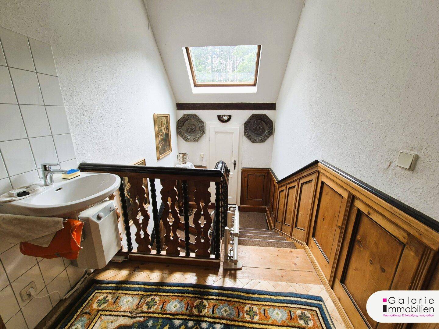 Treppenhaus mit Holzgeländer, Oberlicht und einem Waschbecken im oberen Bereich.