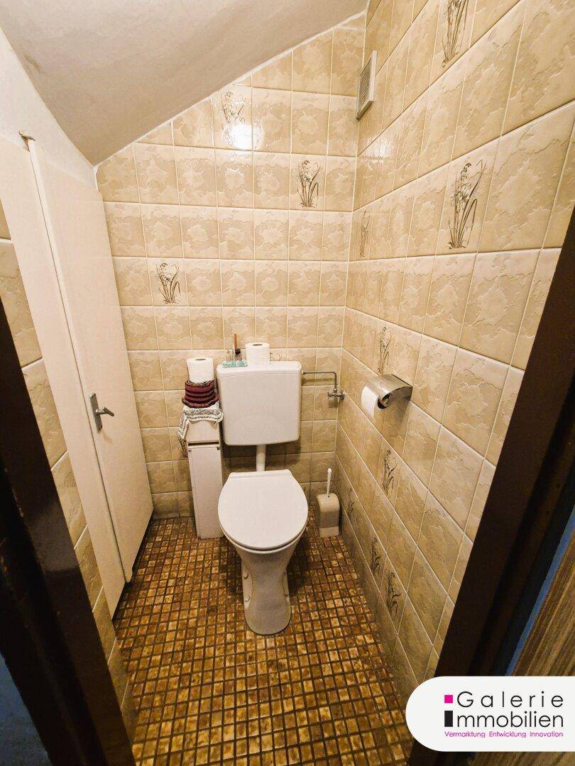 Kleines Gäste-WC mit beigefarbenen Fliesen und einem wandmontierten WC.