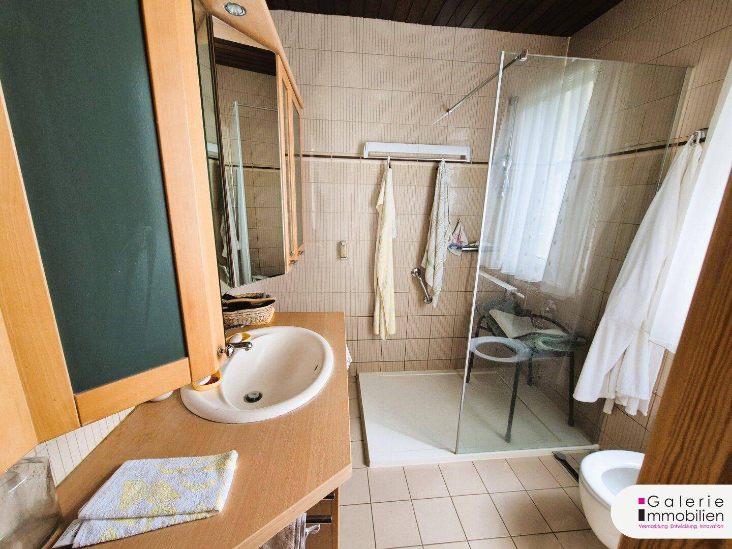Badezimmer mit beigefarbenen Fliesen, Einzelwaschbecken und einer modernen Glasdusche.