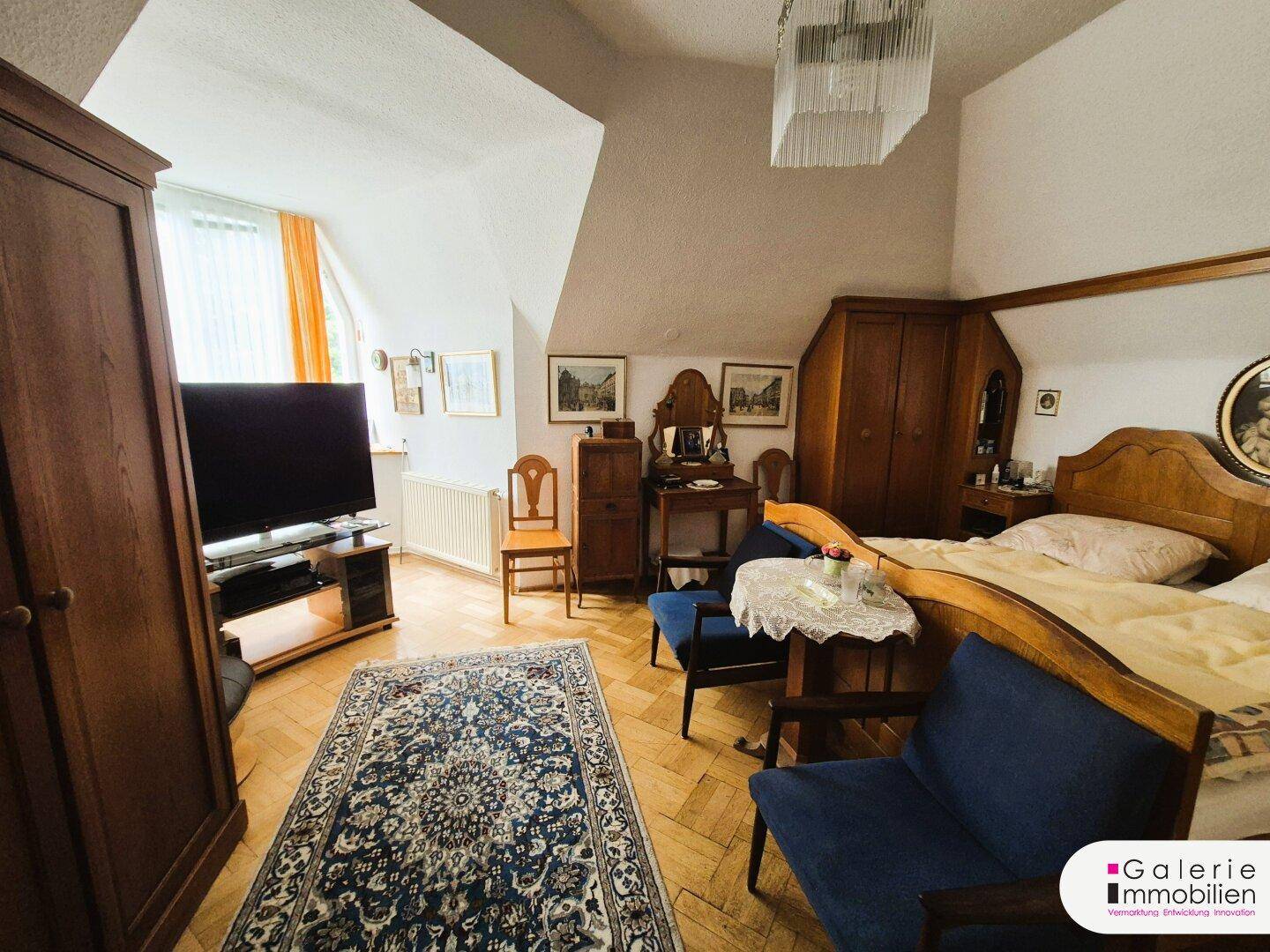 Geräumiges Schlafzimmer mit Dachschrägen, Parkettboden und traditionellen Holzmöbeln.