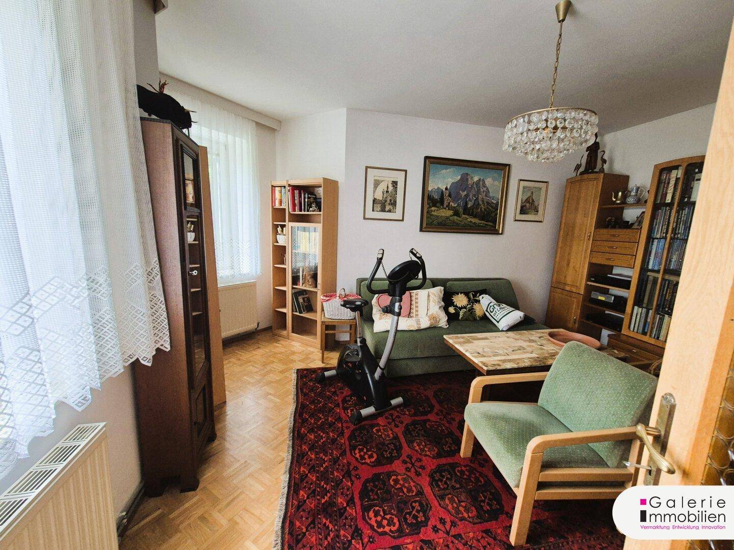 Gemütliches Wohnzimmer mit Parkettboden, Sofa, Bücherregalen und einem Kachelofen.