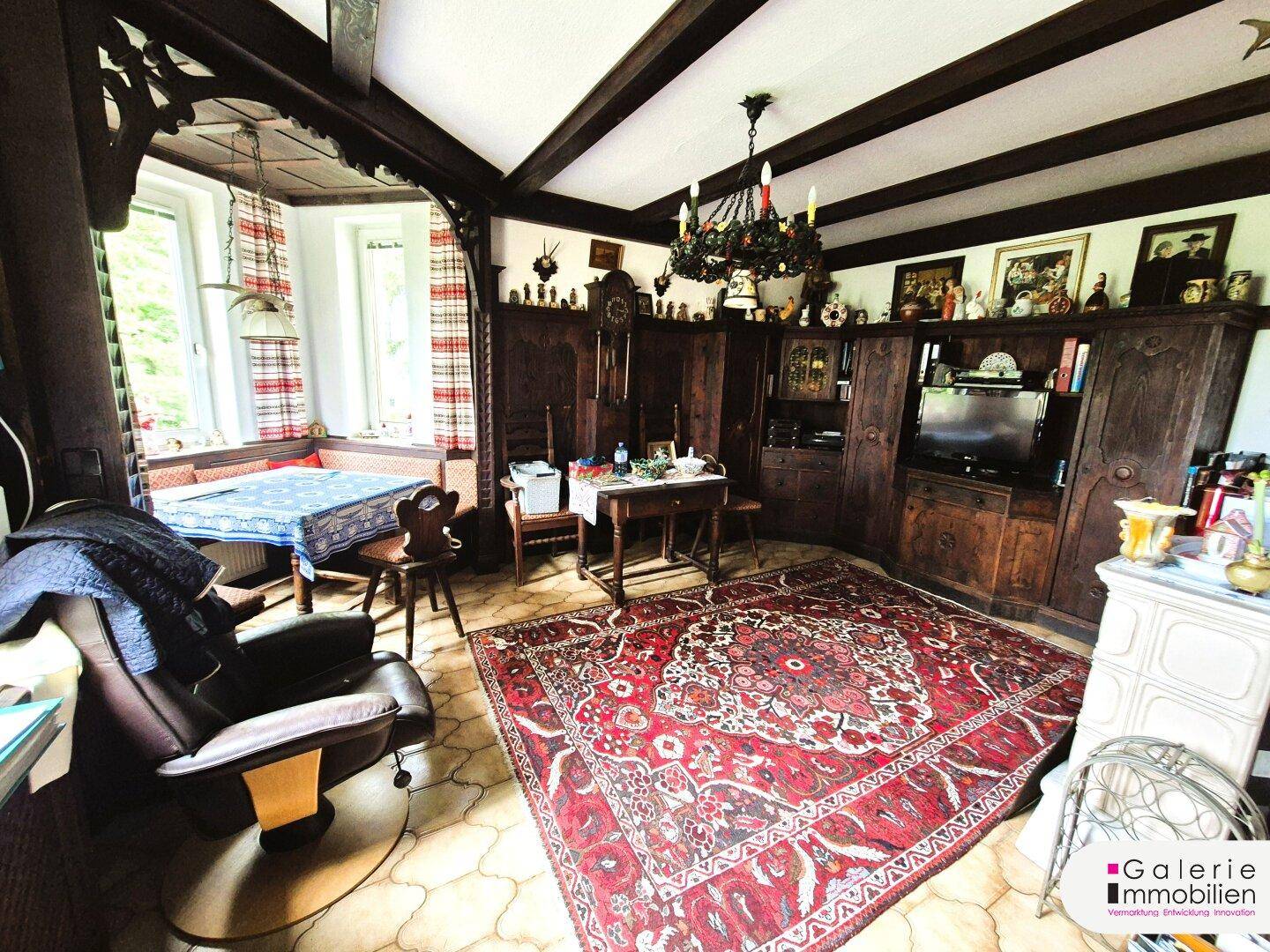Rustikales Wohnzimmer mit Holzbalkendecke, traditionellen Möbeln und einem großen Orientteppich.
