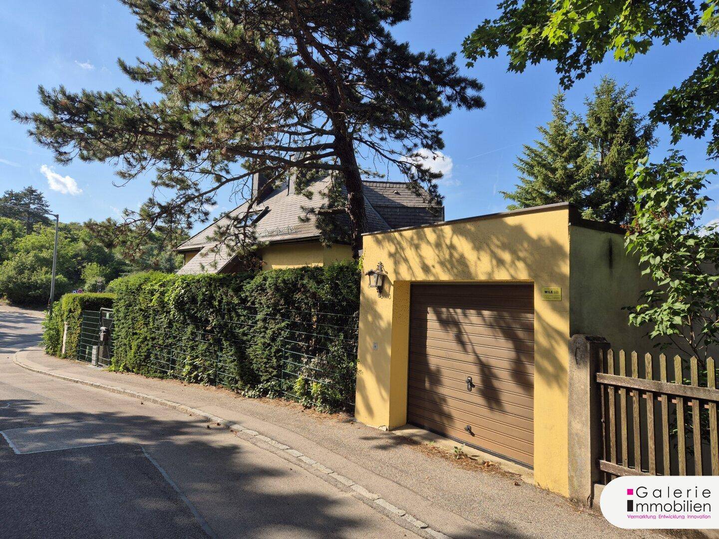 Ansicht von der Straße mit einer Garage, einer hohen Hecke und dem dahinterliegenden Haus.