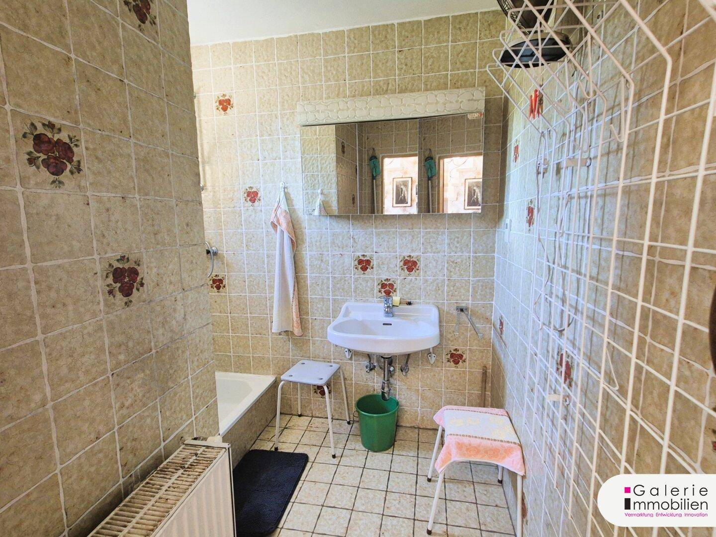 Badezimmer mit beigefarbenen Fliesen, Waschbecken, Badewanne und Heizkörper.
