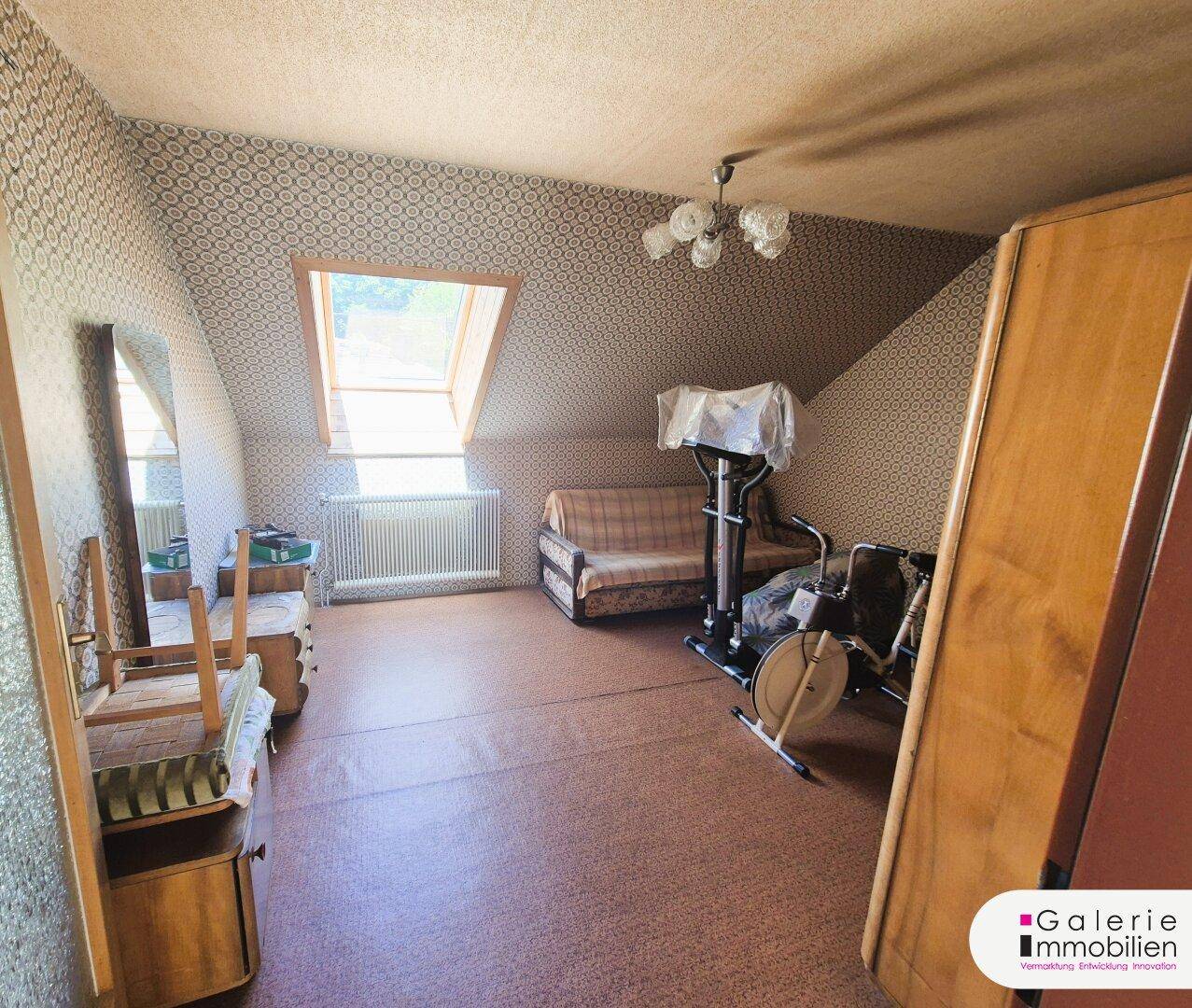 Dachzimmer mit Dachfenster, Heizkörper und Stauraum, derzeit als Abstellraum genutzt.