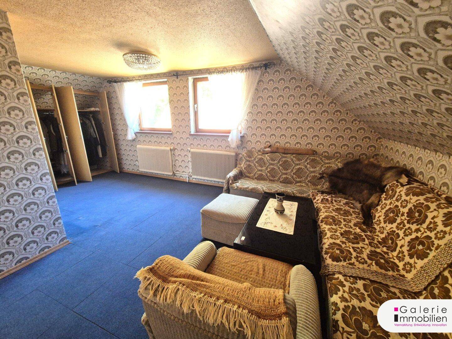 Gemütliches Dachwohnzimmer mit blauer Teppichboden, Sofa und traditioneller Einrichtung.