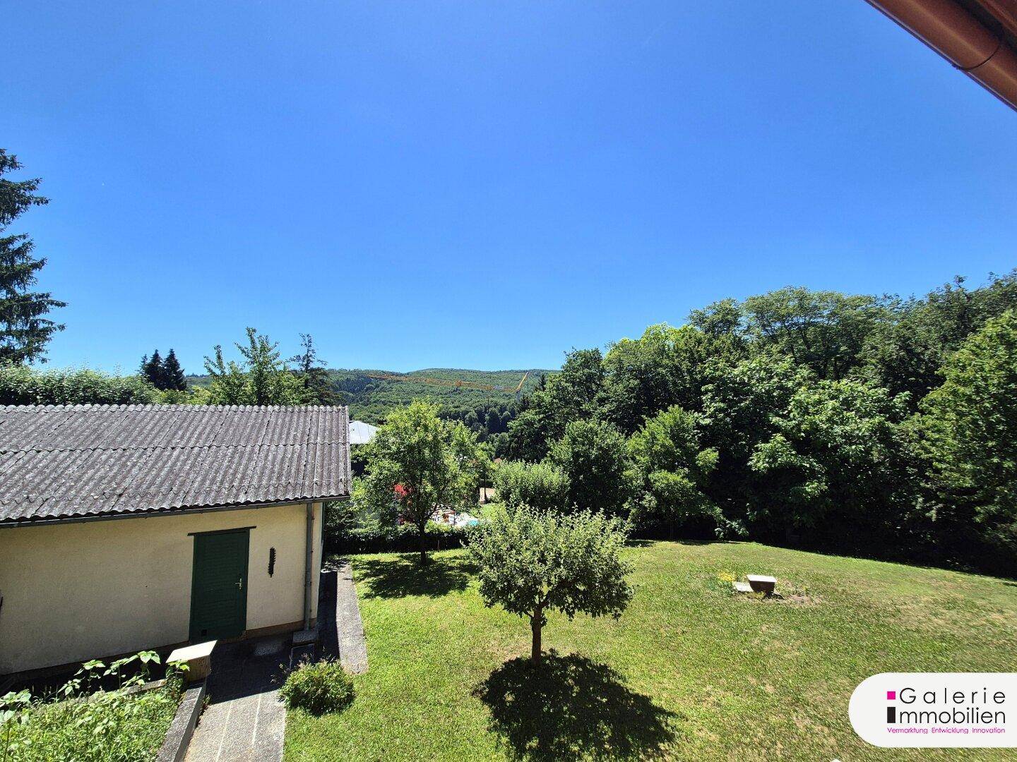 Weitläufiger Garten mit Rasenfläche, Bäumen und einem Nebengebäude an einem sonnigen Tag.