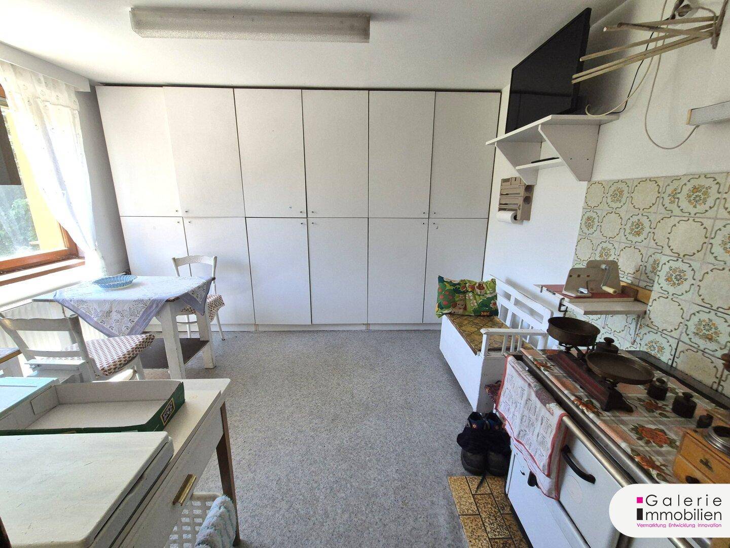 Vielseitiger Raum mit Einbauschränken, kleinem Tisch und einem alten Holzofen.