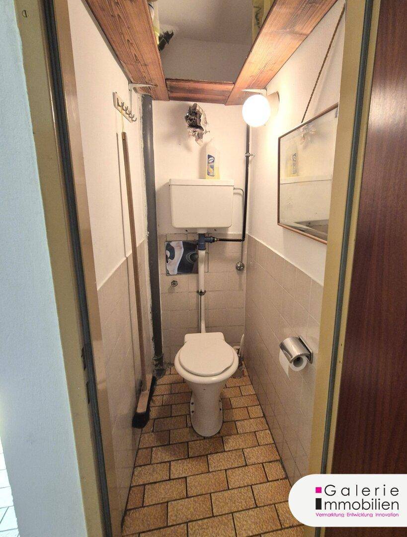 Kleines separates WC mit Fliesenboden und einfacher Ausstattung.