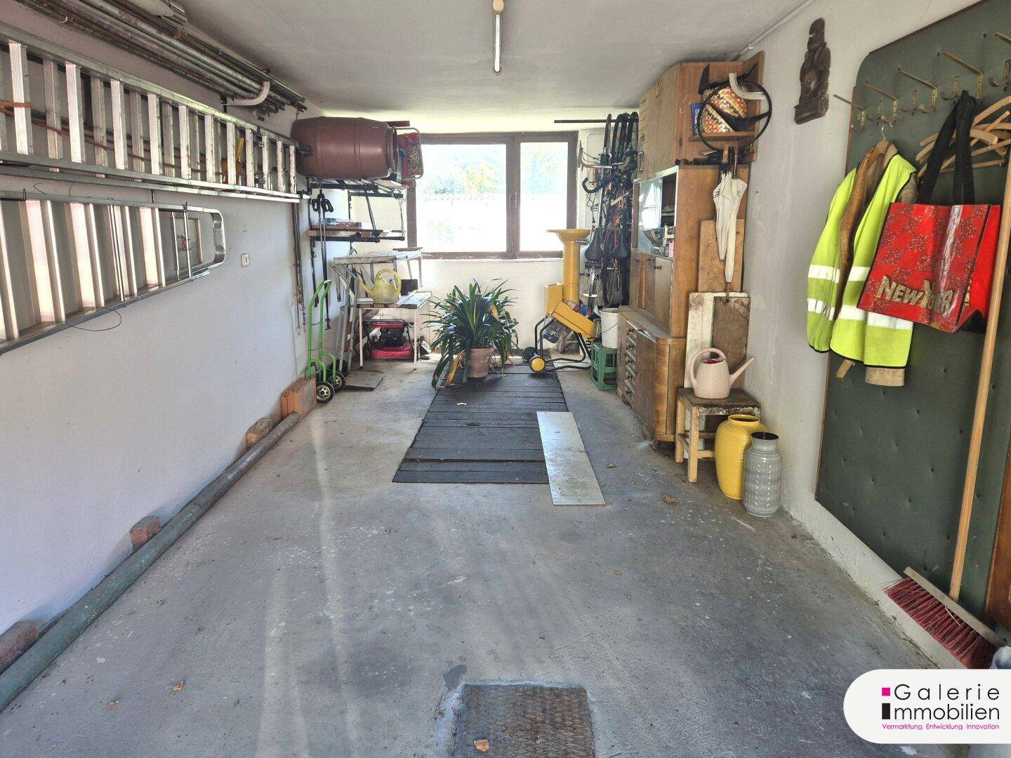 Geräumige Garage oder Werkstatt mit Fenster, Betonboden und Stauraum für Werkzeuge.