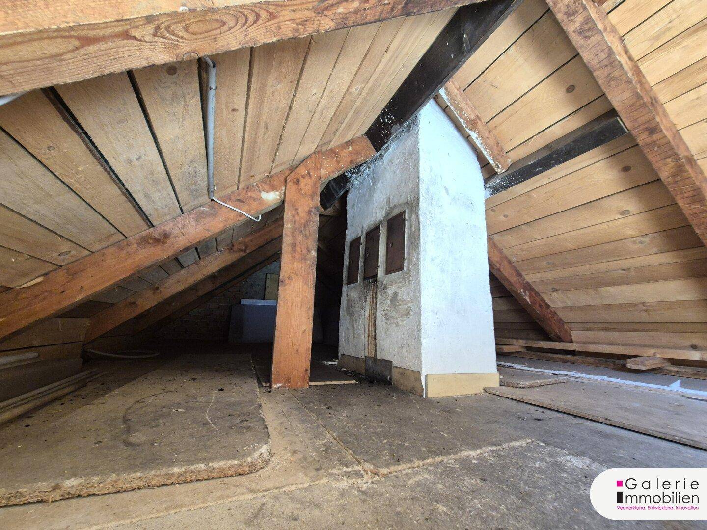 Unausgebauter Dachboden mit sichtbaren Holzbalken und einem gemauerten Kaminzug.
