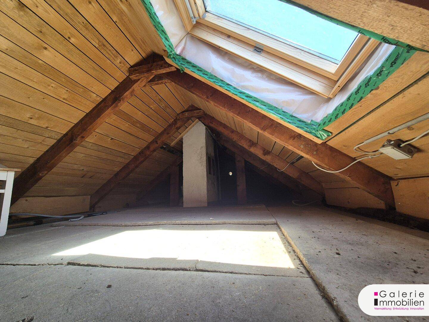 Helles Dachgeschoss mit sichtbaren Holzbalken und einem Dachfenster für Tageslicht.