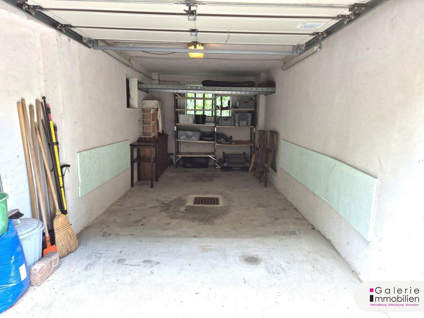 Geräumige Garage mit Betonboden, Stauraum und automatischem Garagentor, ideal für Fahrzeuge und Lagerung.
