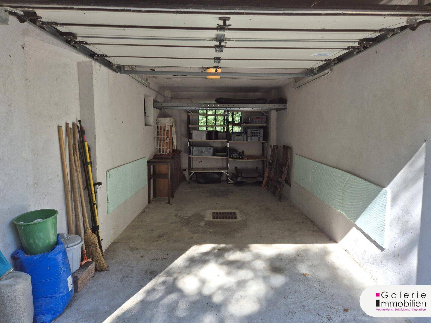Geräumige Garage mit Rolltor und Stauraum für Werkzeuge und Geräte.
