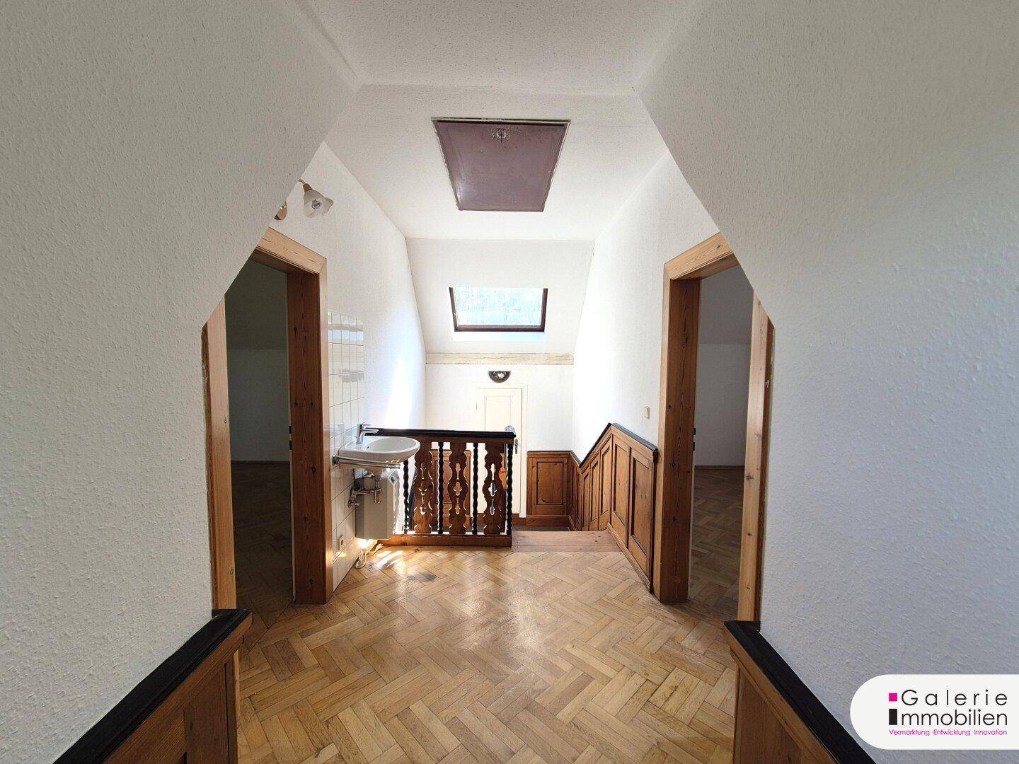 Heller Flur im Obergeschoss mit Holzparkett, Dachfenster und kleinem Waschbecken.