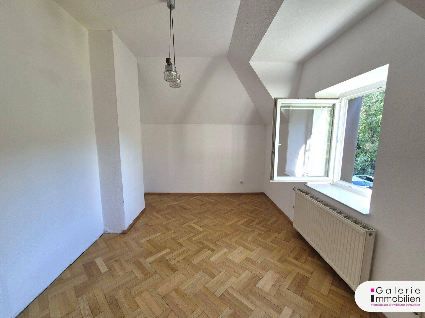 Helles Zimmer mit Fischgrätparkett, Dachschräge und großem Fenster.