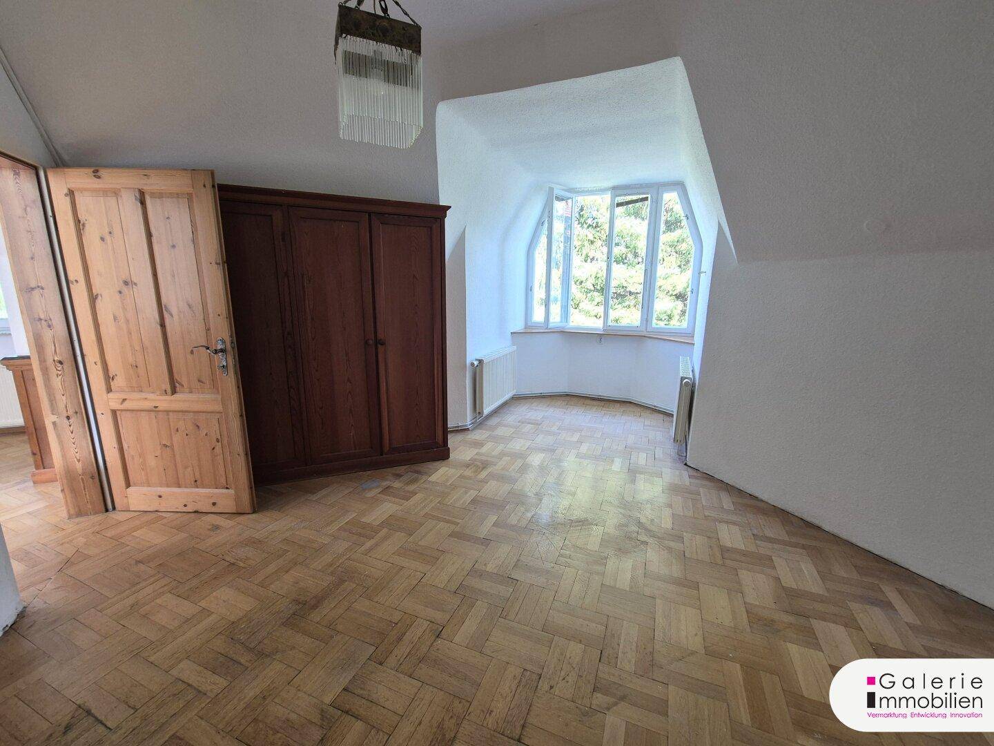 Geräumiges Schlafzimmer mit Parkettboden, Dachschräge und großem Erkerfenster.