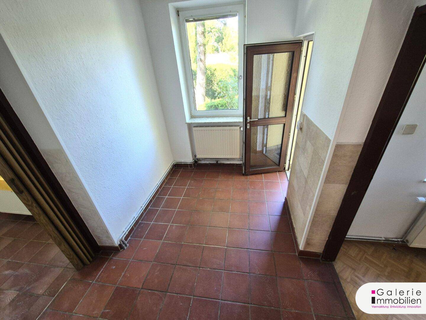 Eingangsbereich mit Terrakottafliesen und Zugang zum Garten durch eine Glastür.