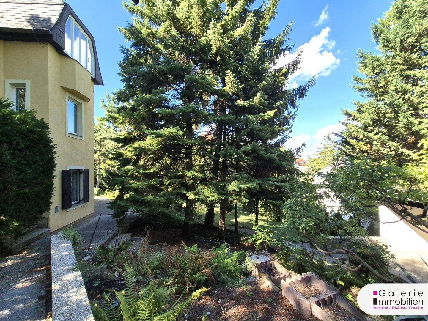 Gelbe Hausfassade mit Mansarddach und großem Gartenbereich.