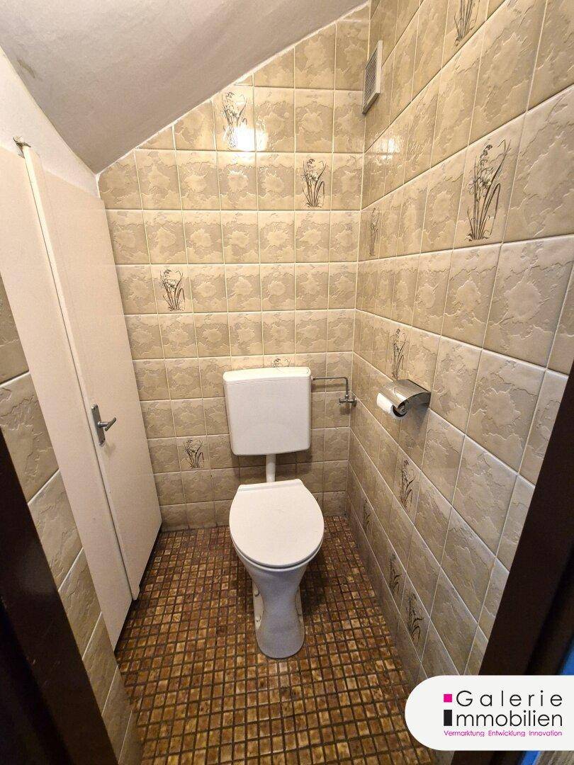 Kleines Gäste-WC mit WC, Fliesen an den Wänden und gemustertem Boden.