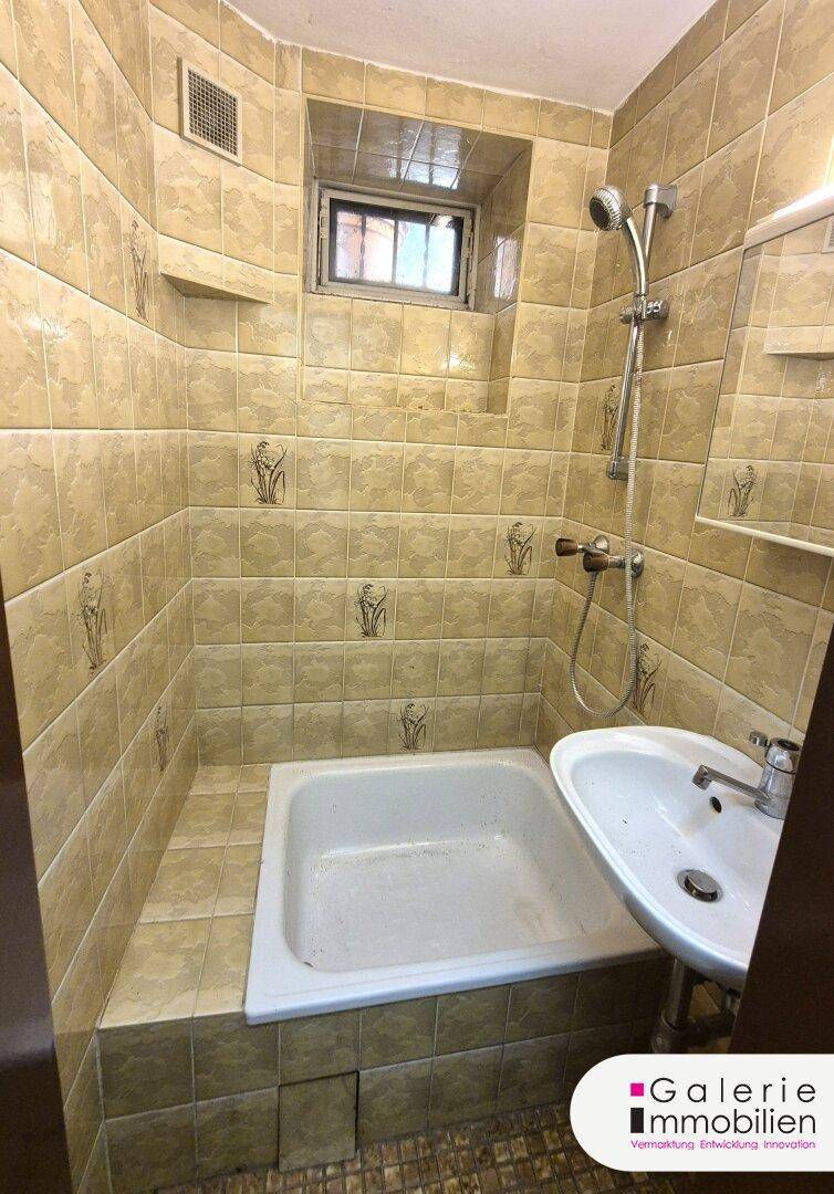 Kleines Badezimmer mit Badewanne, Dusche, Waschbecken und Fliesen an Wänden und Boden.