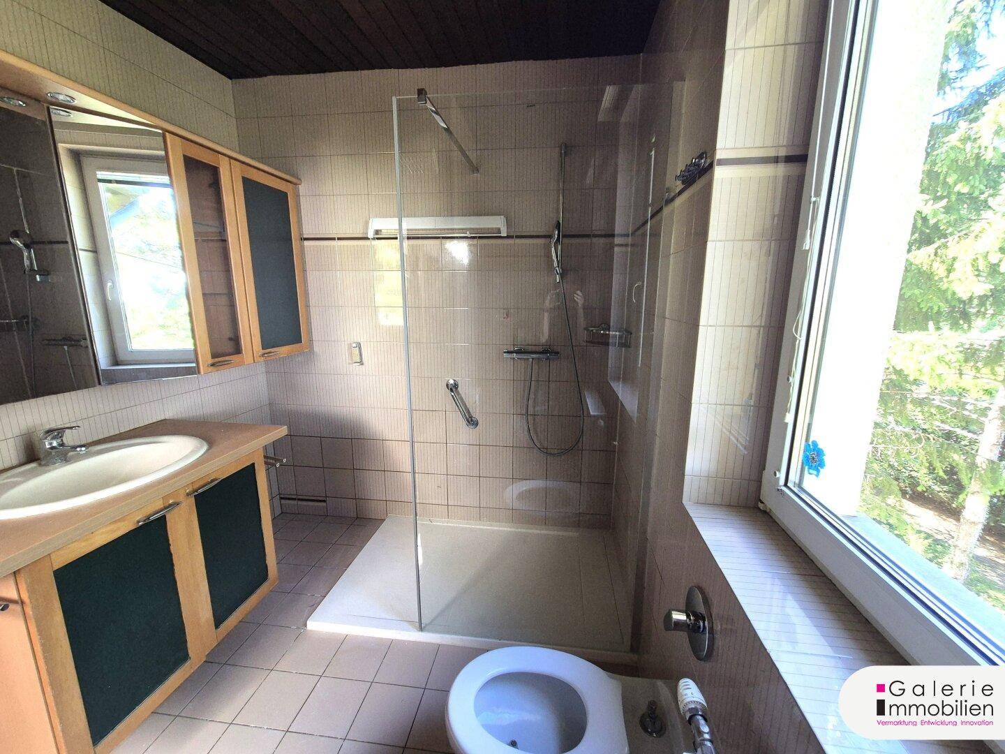 Helles Badezimmer mit begehbarer Dusche, Einzelwaschbecken und Fenster mit Blick ins Grüne.