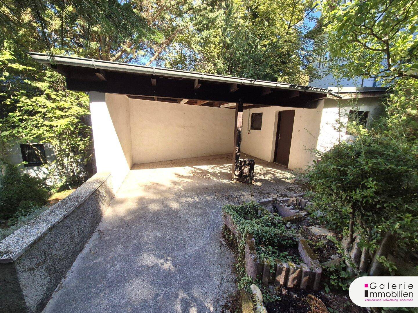 Überdachter Stellplatz oder Carport mit angrenzendem Gartenbereich und viel Grün.