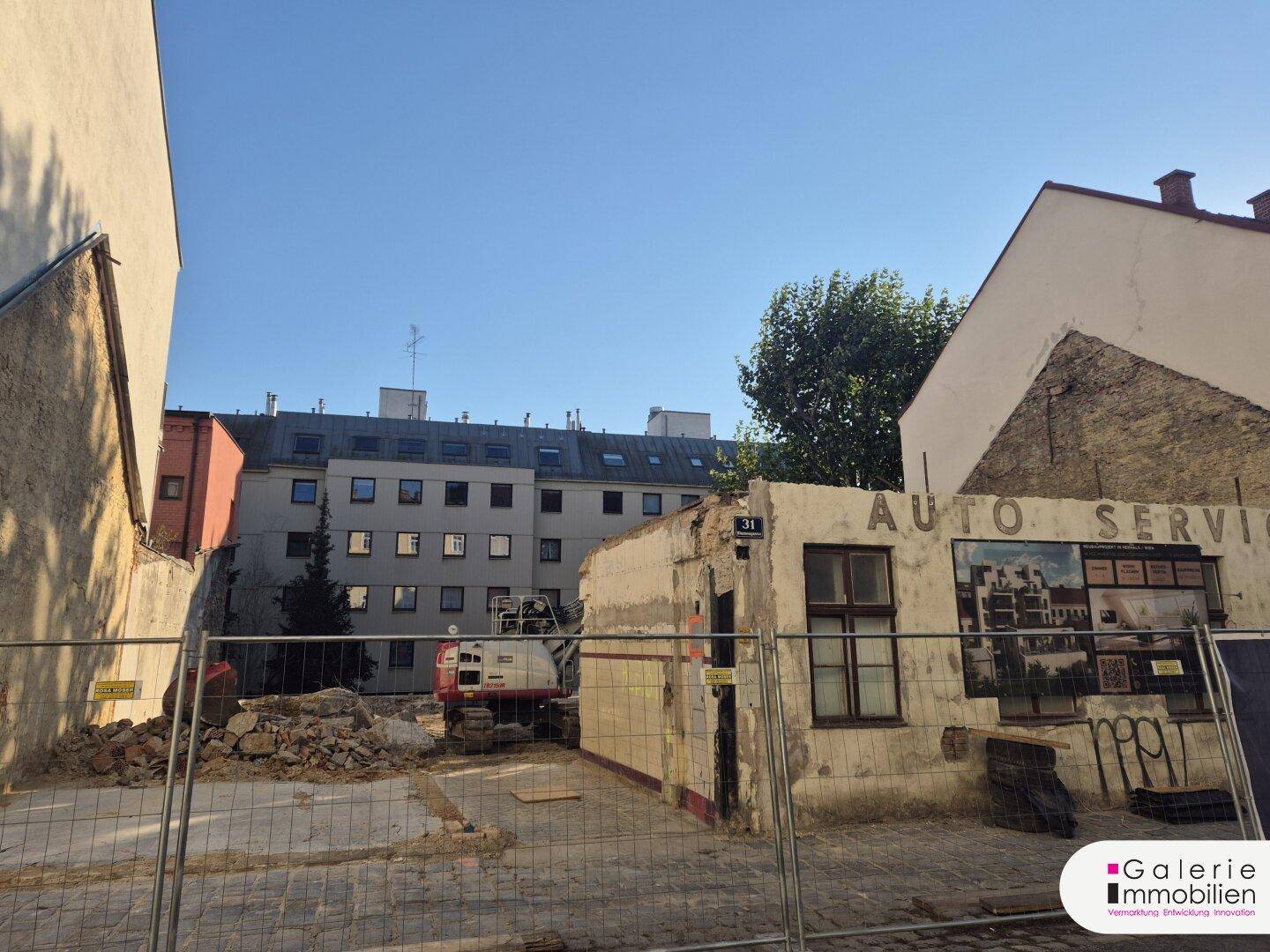 Baustelle mit Schutt und Bagger, umgeben von Bestandsgebäuden, bereit für eine Neubebauung.