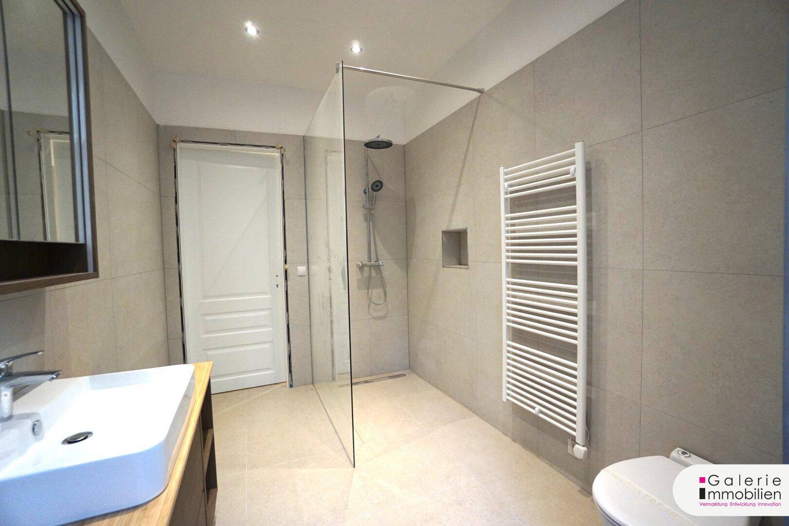 Modernes Badezimmer mit begehbarer Dusche, grauen Fliesen und beheiztem Handtuchhalter.