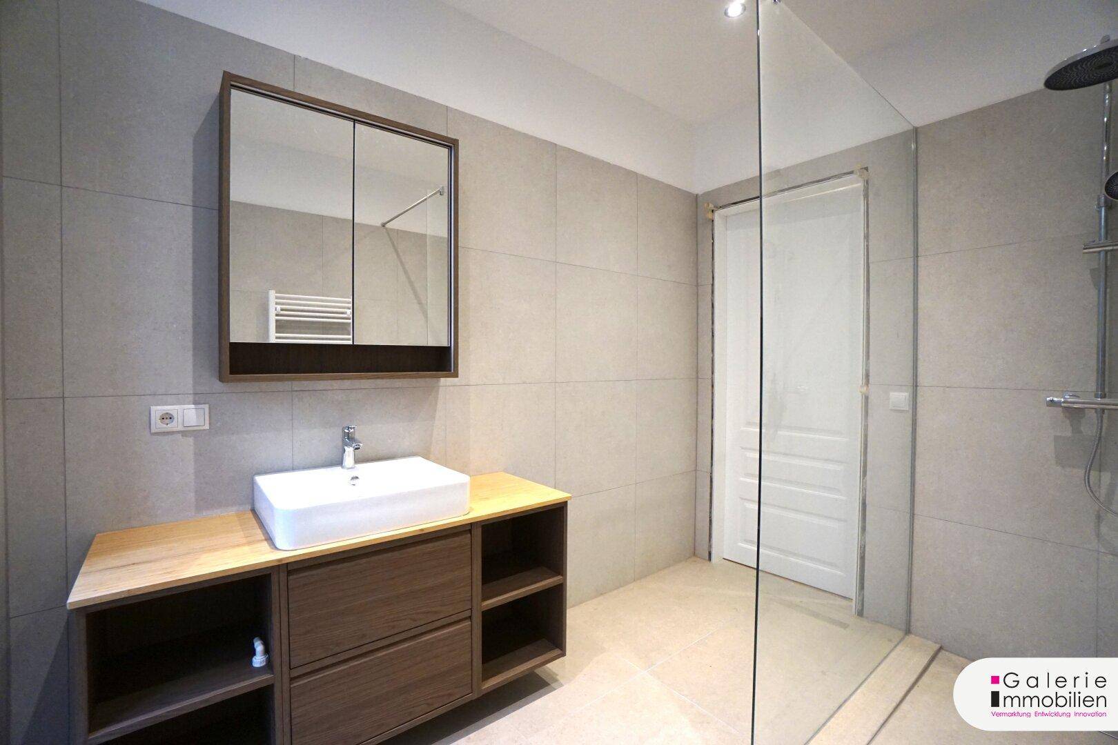 Stilvolles Badezimmer mit modernem Waschtisch, Spiegelschrank und großer begehbarer Dusche.