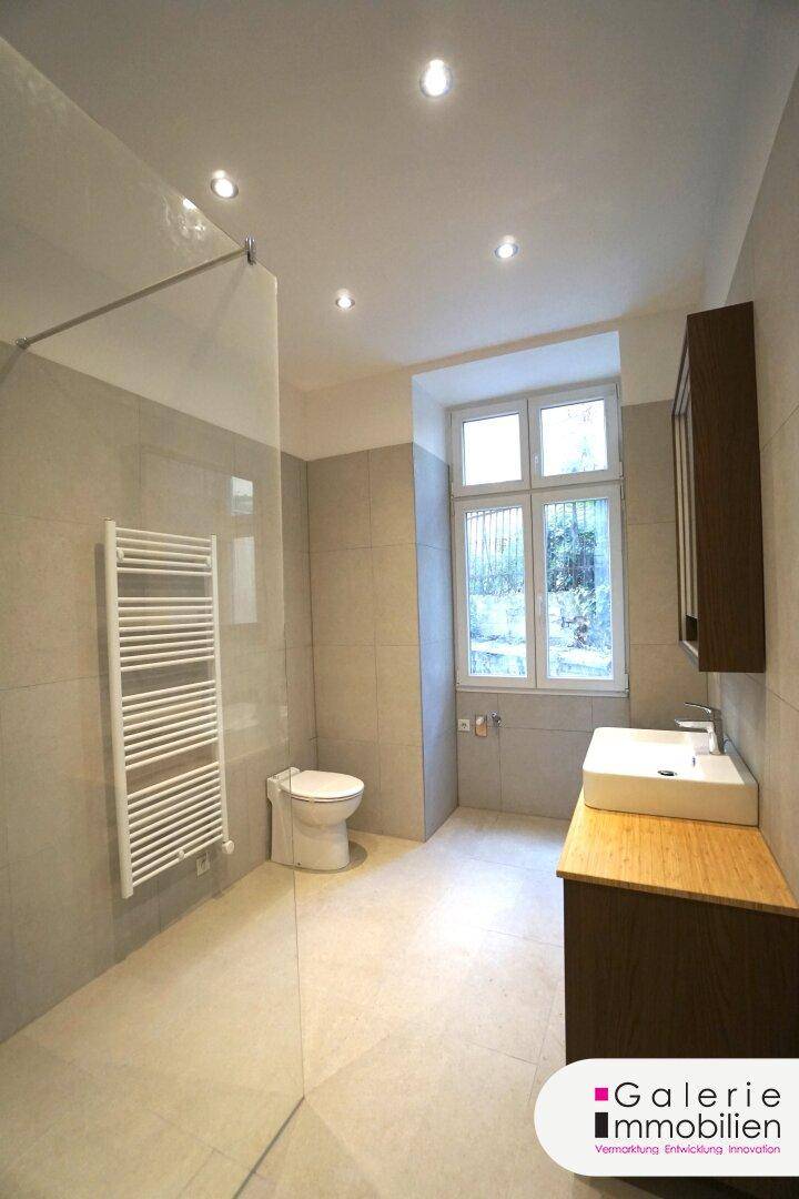 Helles Badezimmer mit Fenster, moderner Dusche, WC und Waschtisch mit Holzunterschrank.