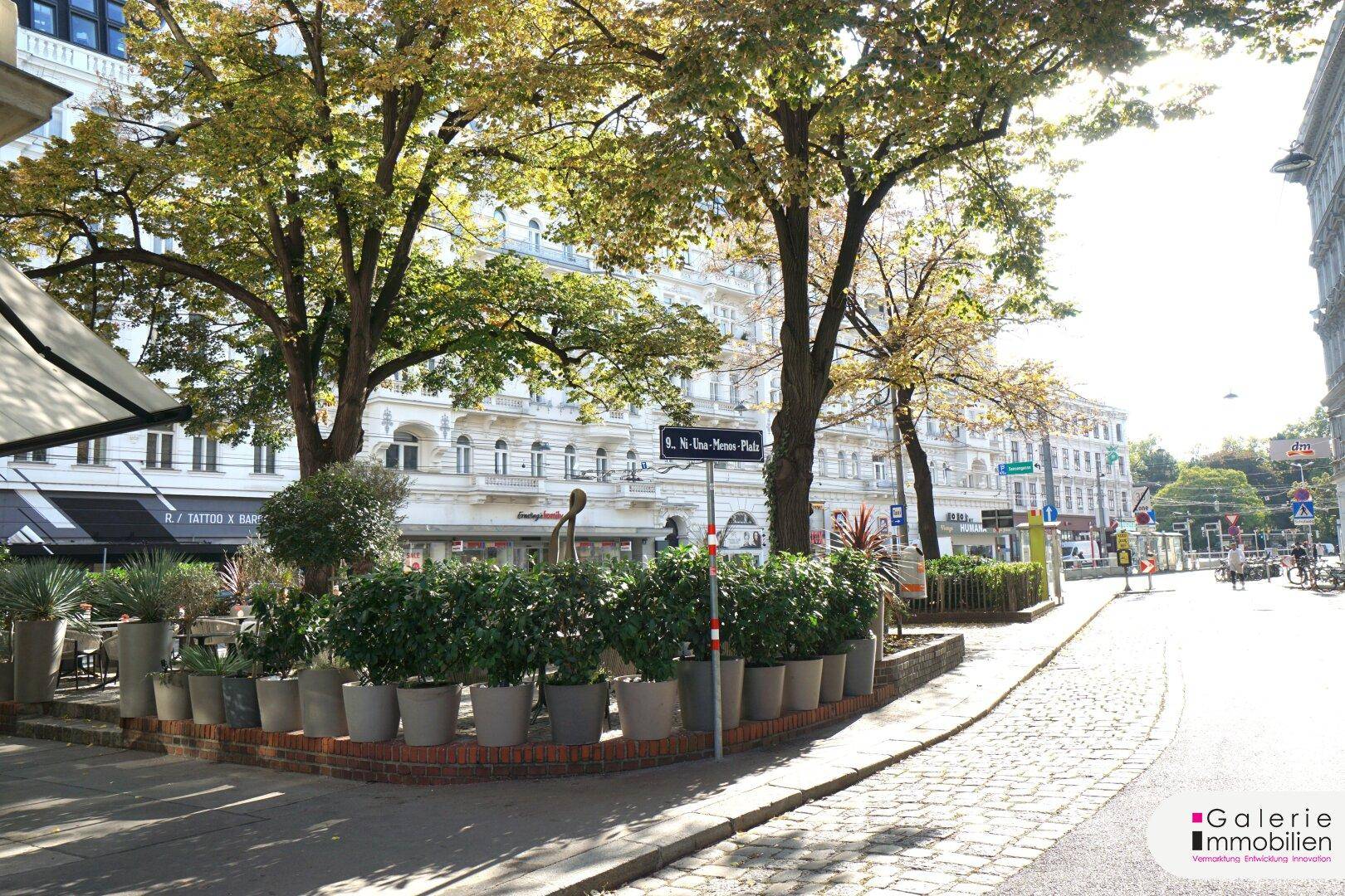 Belebtes Stadtviertel mit Bäumen, Geschäften und Kopfsteinpflaster, das urbanes Flair vermittelt.