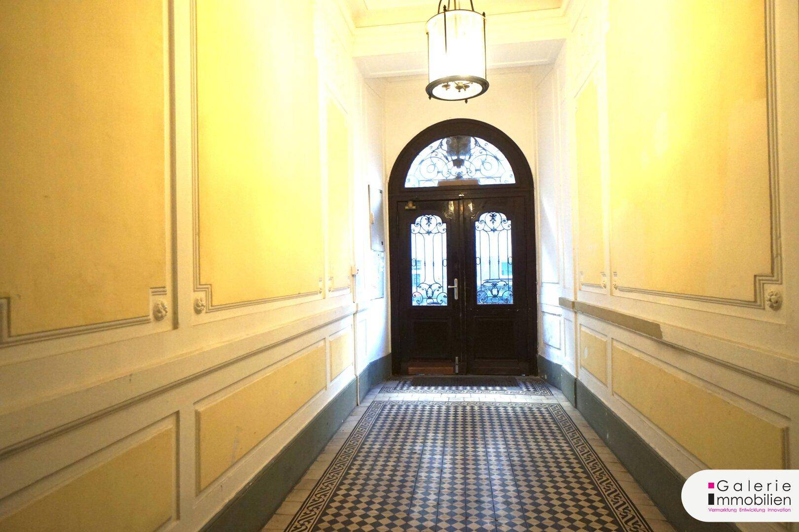 Klassischer Flur mit gemustertem Fliesenboden und einer verzierten Eingangstür in einem Altbau.