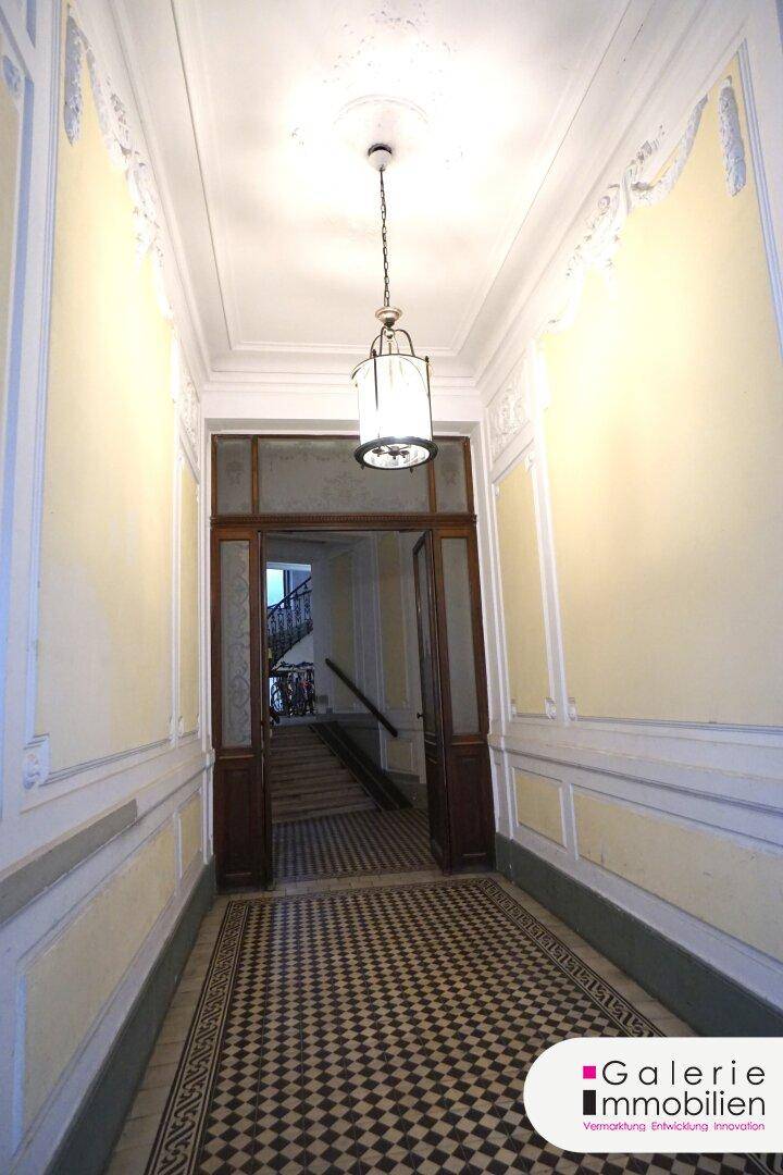 Historischer Eingangsbereich mit hohen Decken, gemustertem Fliesenboden und eleganter Beleuchtung.