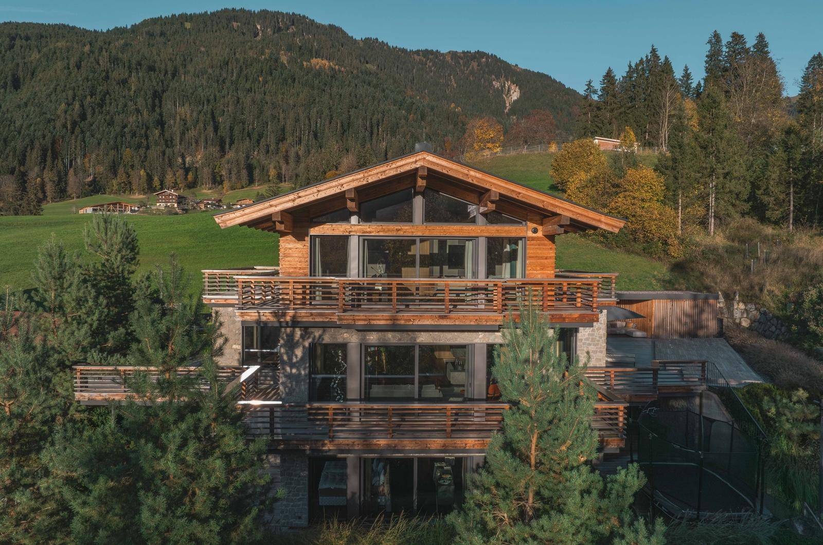 Frontansicht des luxuriösen Chalets mit Holzfassade, großen Glasfronten und umgeben von grüner Natur.