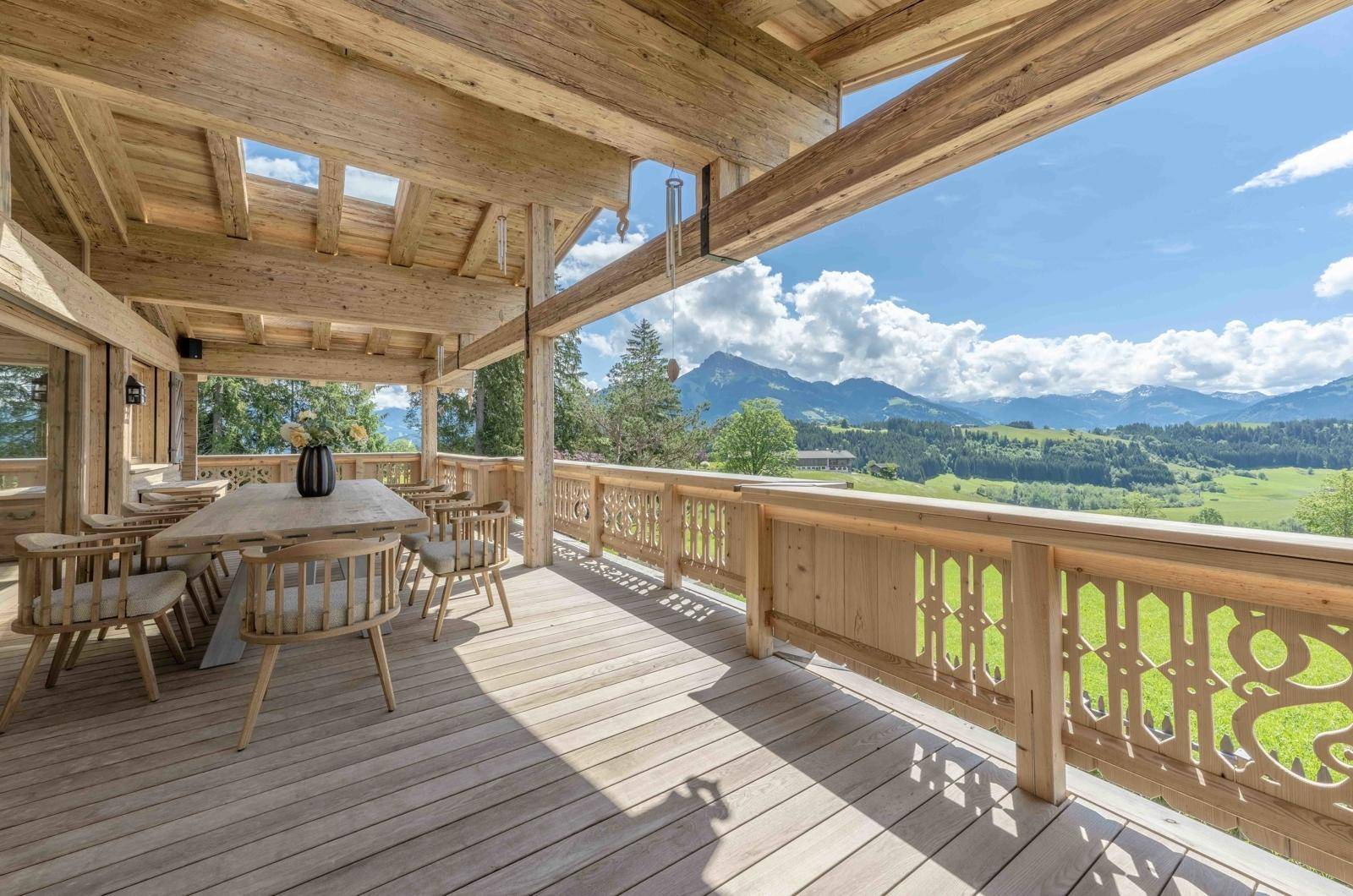 Geräumige Holzterrasse mit Esstisch und Stühlen, die einen weiten Blick auf die Berge bietet.