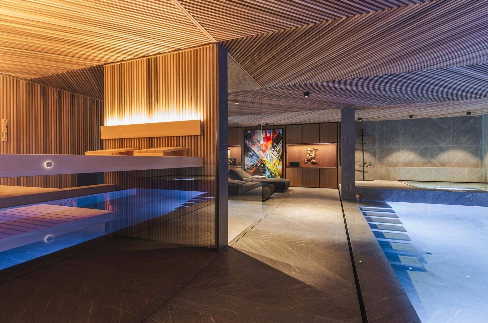 Moderne Sauna mit Holzverkleidung und indirekter Beleuchtung, direkt neben dem luxuriösen Innenpoolbereich.