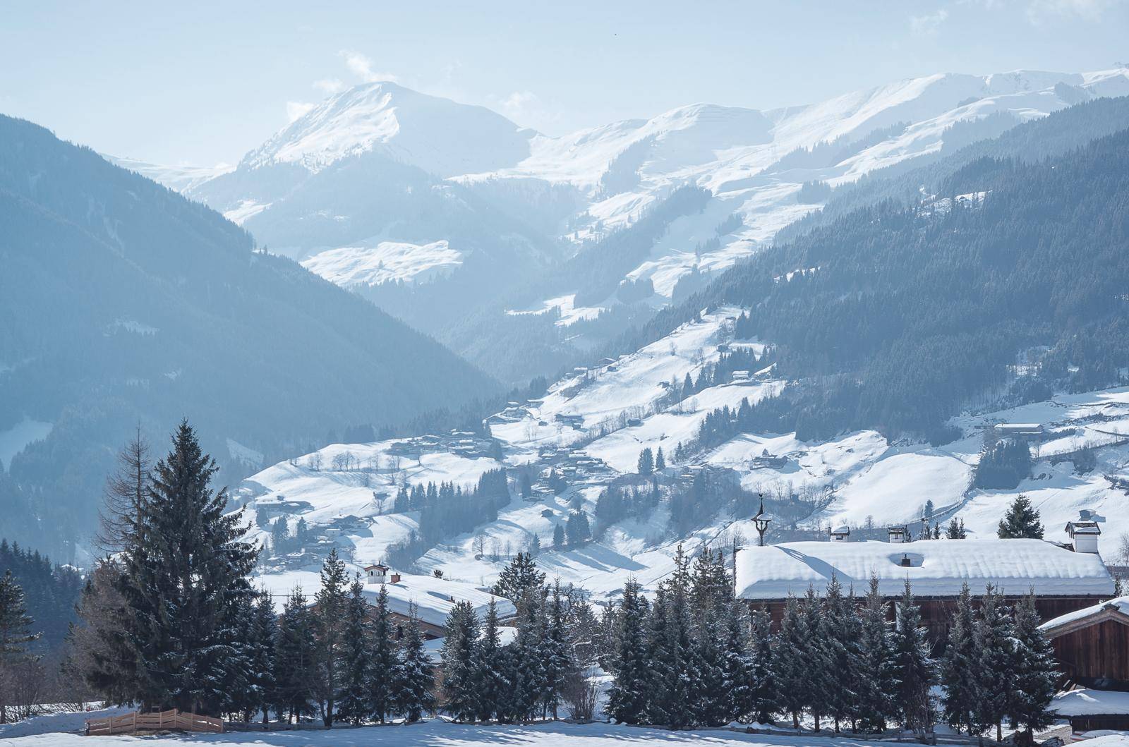 Malerischer Panoramablick auf ein verschneites Bergdorf und die umliegende Alpenlandschaft unter blauem Himmel.