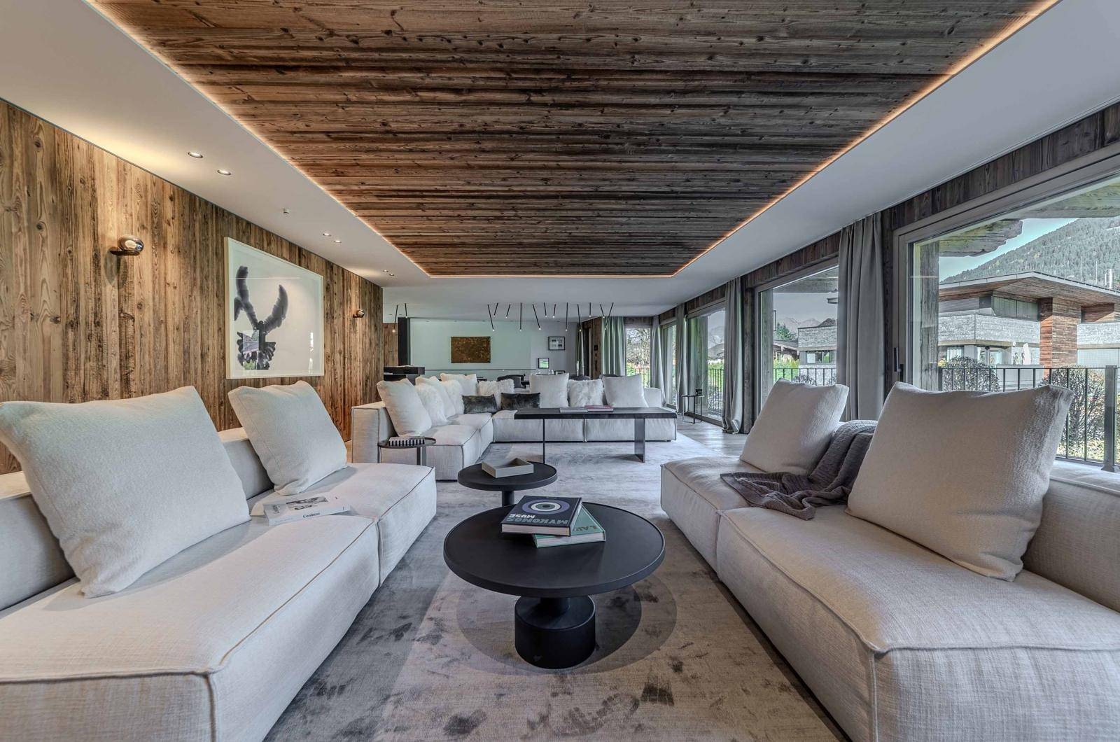 Geräumiges Wohnzimmer mit bequemen Sofas, Holzwänden und weitem Blick ins Grüne.