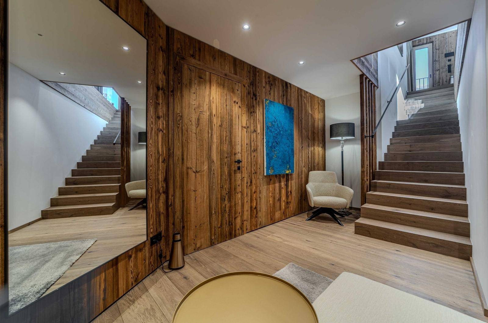 Heller Flur mit Holztreppe, großem Spiegel und moderner Einrichtung.