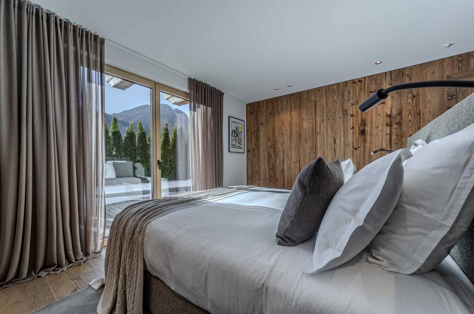 Gemütliches Schlafzimmer mit Holzwand, großem Bett und Zugang zu einem Balkon mit Bergblick.