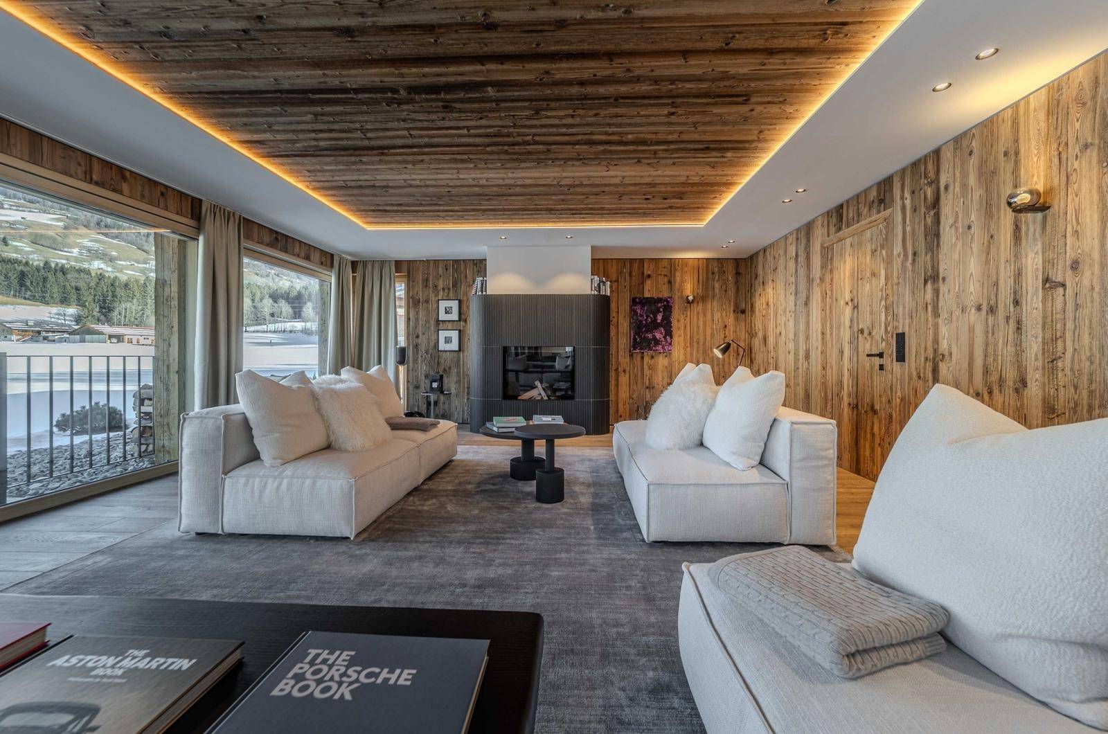 Gemütliches Wohnzimmer mit Kamin, Holzwänden und Blick auf die verschneite Landschaft.