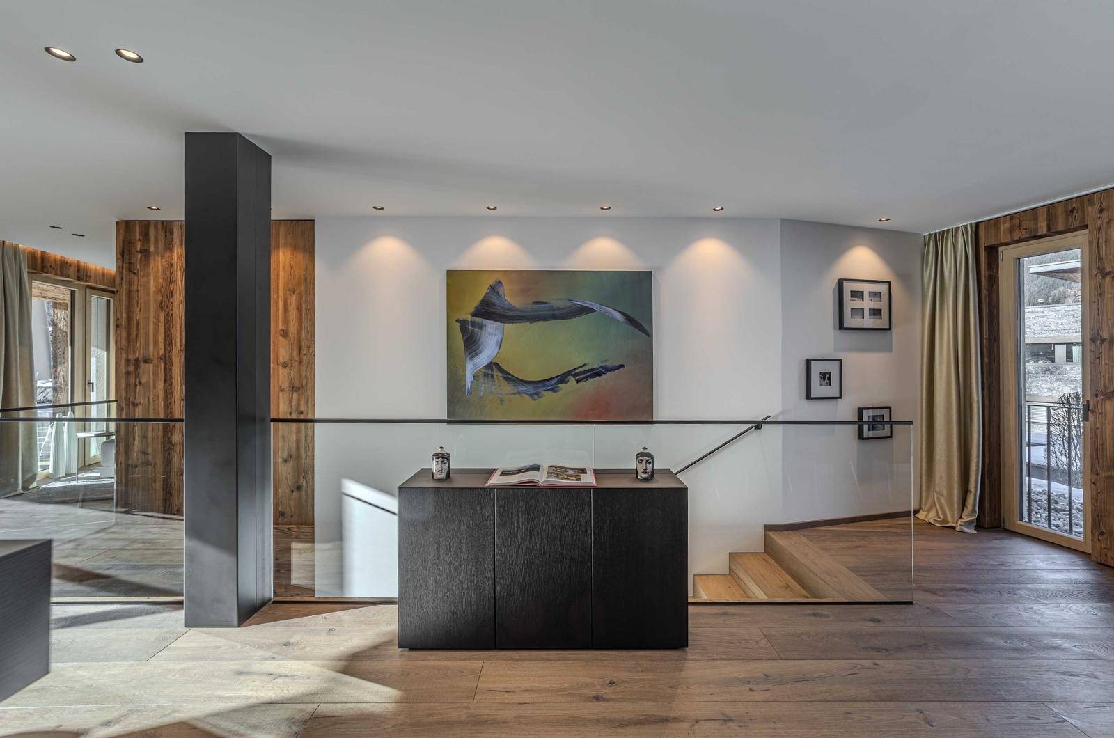 Heller Eingangsbereich mit Holztreppe, Glasgeländer und moderner Kunst.