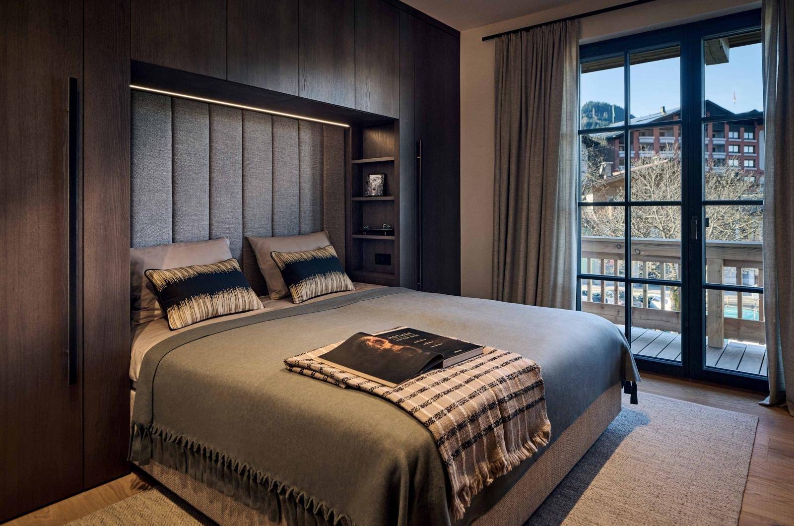 Schlafzimmer mit Einbauschränken, gepolstertem Kopfteil und Balkonzugang mit Bergblick.