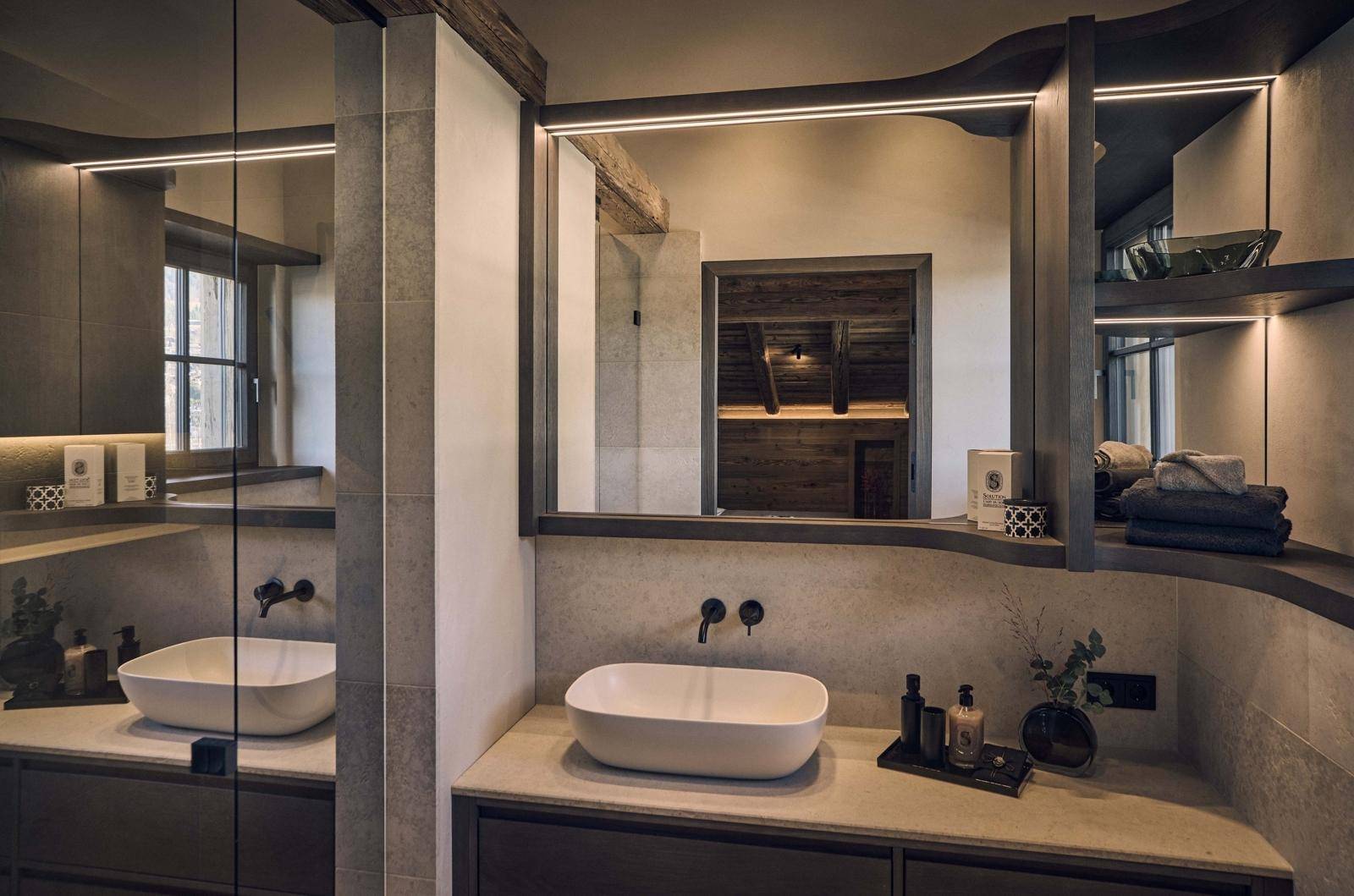 Modernes Badezimmer mit Doppelwaschbecken, Spiegel und Blick auf eine Sauna im Hintergrund.