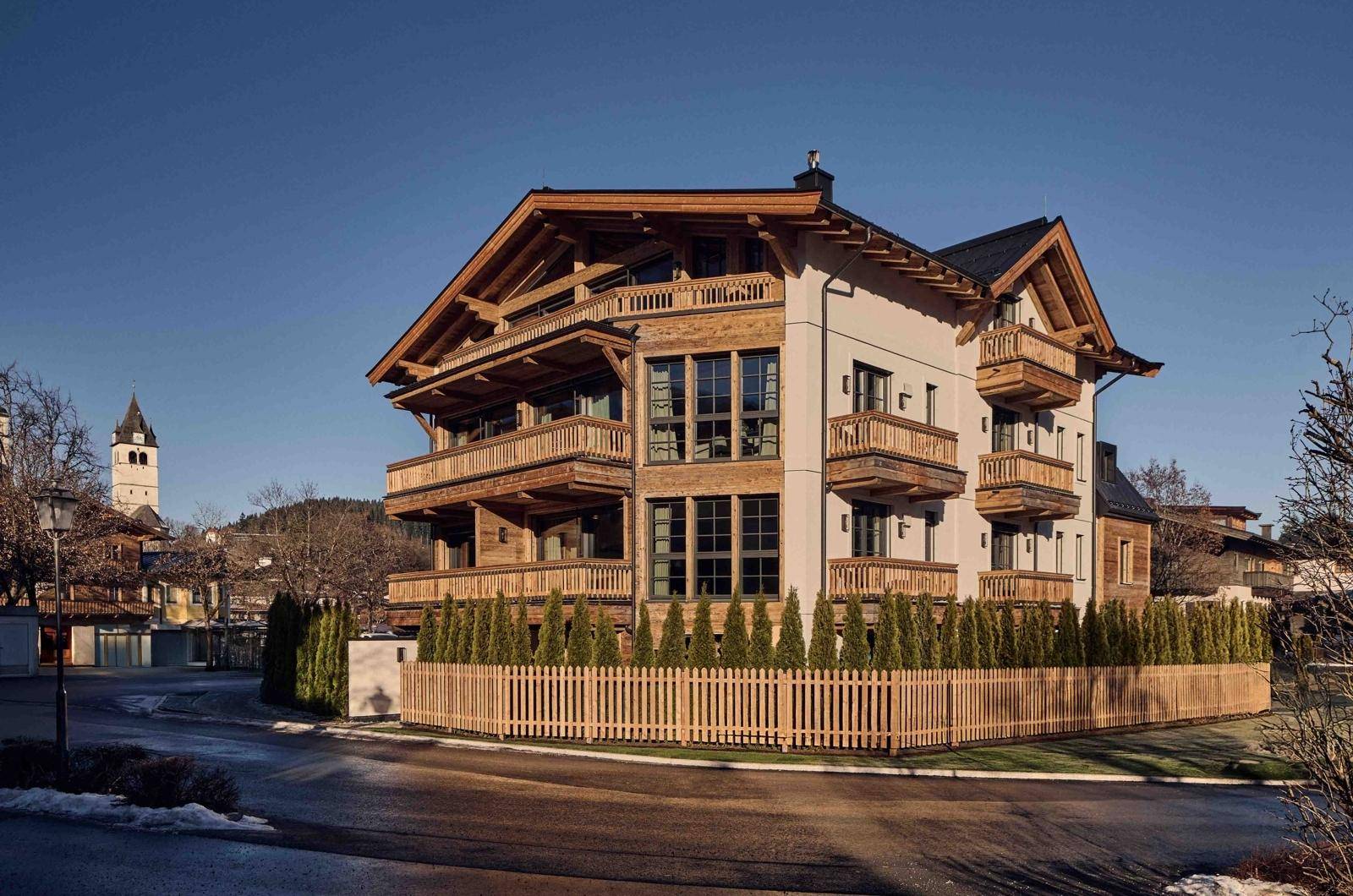 Attraktives Mehrfamilienhaus im alpinen Stil mit Holzfassade und Balkonen unter blauem Himmel.