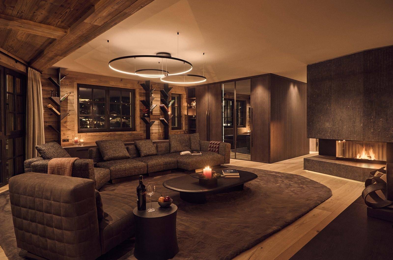 Gemütliches Wohnzimmer mit Kamin, Holzwänden und moderner Beleuchtung in warmer Atmosphäre.