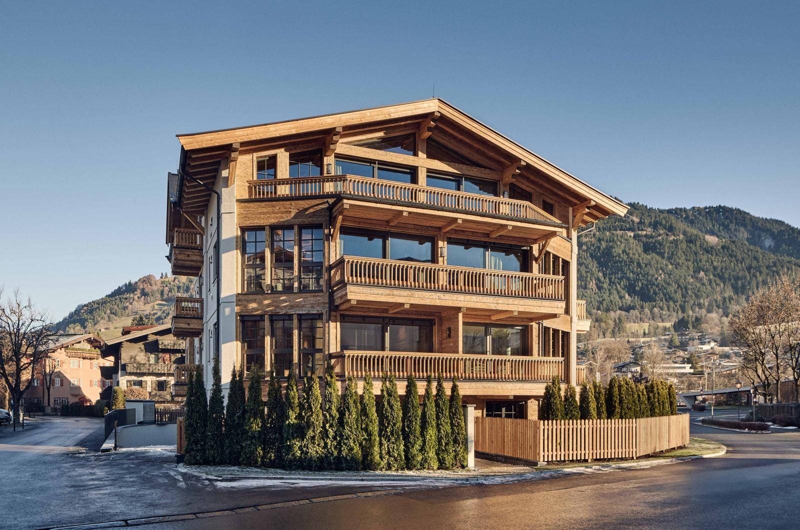 Modernes Gebäude im alpinen Stil mit Holzverkleidung und Balkonen in einer Berglandschaft.